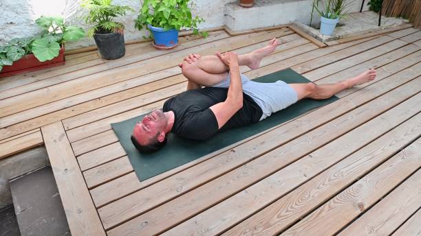 istock Man practicing yoga on a wooden deck, performing a stretch exercise on a mat surrounded by potted plants for a peaceful setting 2170688396