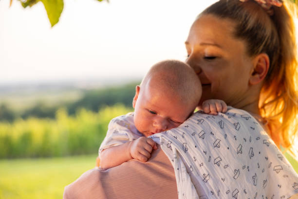 Side view of Affectionate Mother with Blond Hair Carrying Adorable Newborn Son in Park with Sky in the Background during Summer