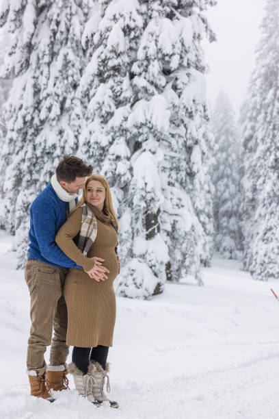 istock Couple Touching Pregnant Belly while Standing in Snowy Forest 2170691611
