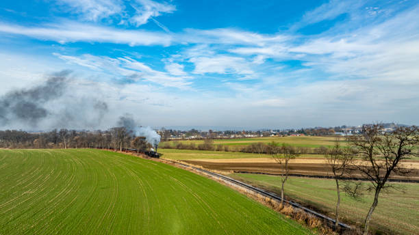 istock Smoke Rises From a Train Traveling Through Green Fields on a Clear Day Near a Small Town 2170696151