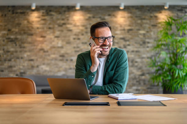 istock Happy financial advisor in glasses communicating over mobile phone while working over laptop at desk 2170700187