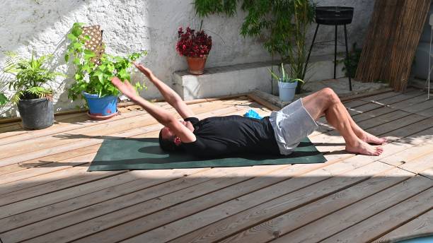 istock Man practicing yoga outdoors on a sunny day, stretching on a wooden deck surrounded by plants and greenery for relaxation and fitness. 2170723531