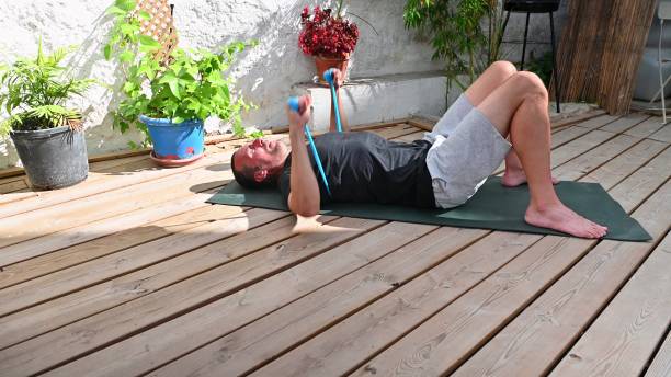 istock Man practicing a resistance band workout on wooden deck surrounded by potted plants in a sunny garden setting 2170723554
