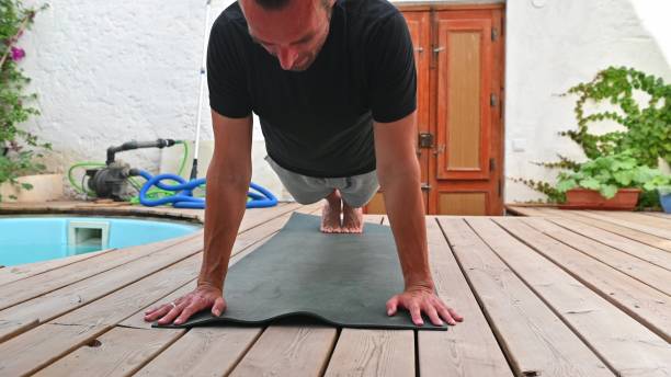 istock Man exercising in plank position on yoga mat outdoors, strengthening core and improving fitness in serene backyard setting on wooden deck 2170723575