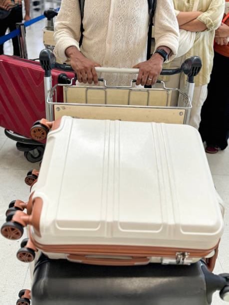 Stock photo showing close-up view of a luggage cart piled with suitcases being wheeled through an airport departure area.\n\n* Not AI modified *