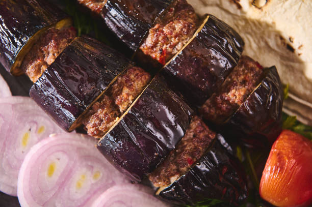 Roasted eggplant and meat kebab with sliced onions and a side of tomato on a platter, showcasing a traditional Middle Eastern cuisine dish with rich, savory flavors.