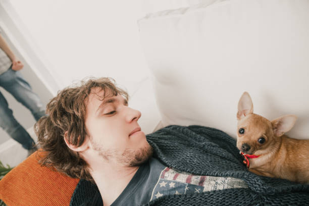 istock Young man relaxing on sofa with small dog as person walks by 2170739131