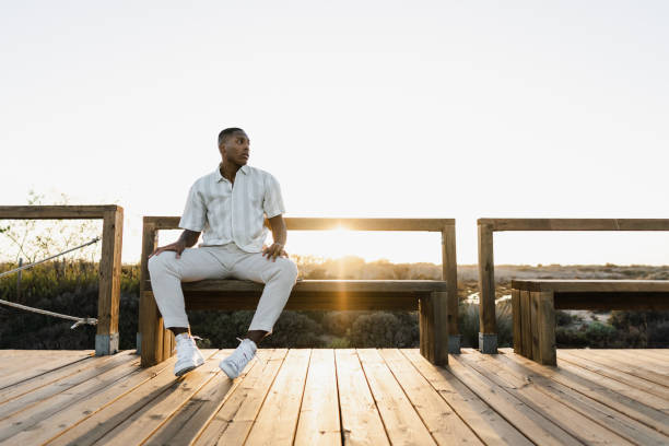 Stylish man sitting on a bench enjoying sunset at the beach