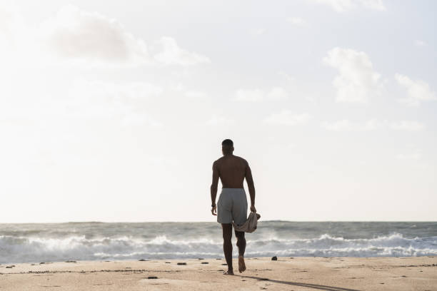istock Athletic man walking on beach at sunset holding towel 2170742643