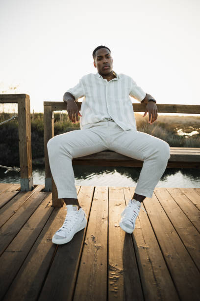 istock Stylish man sitting on a wooden bridge at sunset 2170742662