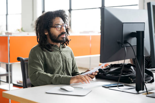 istock Mid adult man with beard and glasses using desktop computer in office, concentrating 2170747734