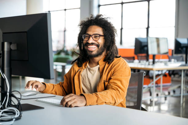 istock Cheerful office worker with beard, wearing casual shirt, at desk using computer 2170747769