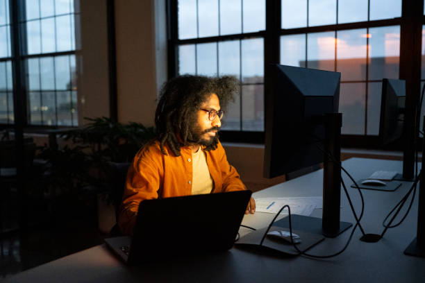 istock Mid adult man working late on computer by window in office 2170747812