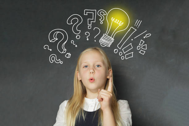 istock Smart child girl student with yellow light bulb and question marks on school blackboard background. Creativity, education and idea concept 2170748326
