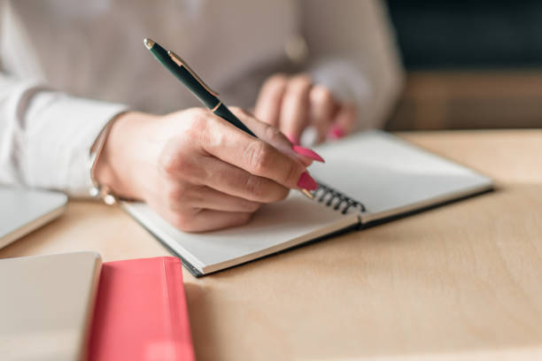 istock A woman's hand writes in a notebook with a pen, sitting at a desk 2170748519