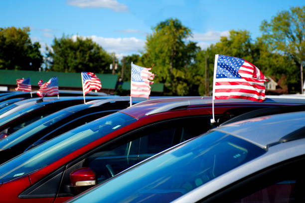 A row of small US flags flying of car for sale at a used car business.