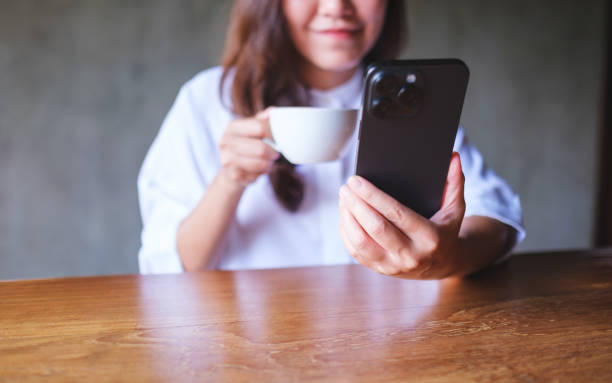 istock Closeup image of a young woman holding and using mobile phone while drinking coffee in cafe 2170772437