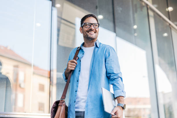 istock A handsome, cheerful, smiling man walking by a building, carrying a laptop. 2170783704
