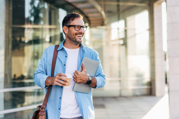 istock A handsome, cheerful, smiling man walking by a building, carrying a laptop. 2170784197