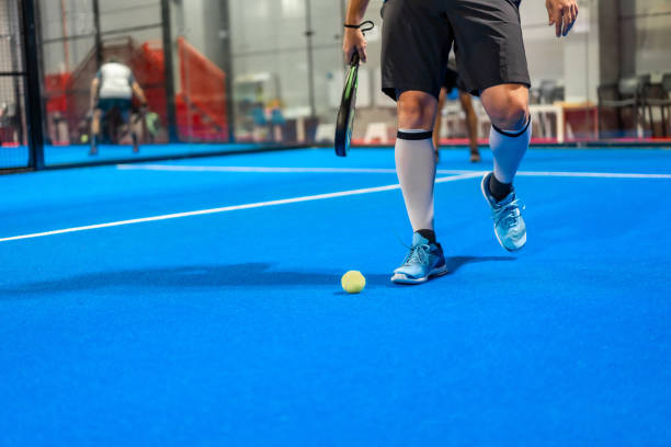 Sportive mature man picking up a paddle ball from the ground in an indoor blue court