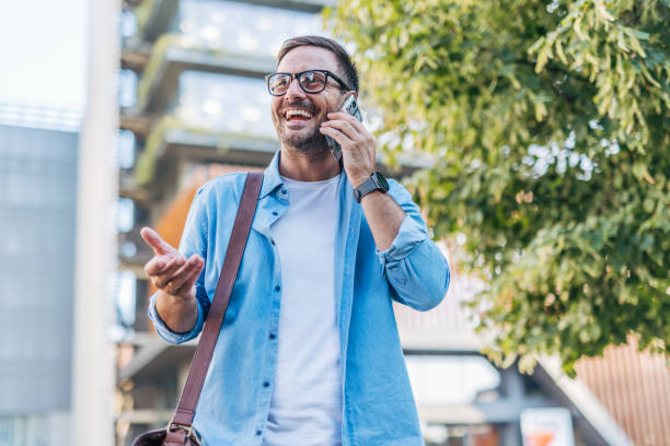 istock A handsome, cheerful, smiling man walking by a building, using smartphone. 2170786631