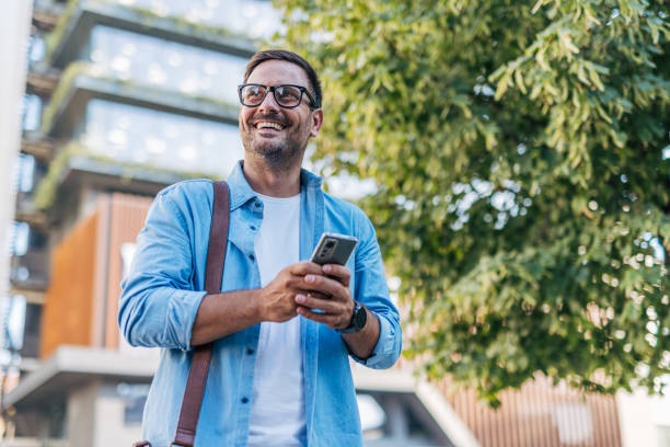 istock A handsome, cheerful, smiling man walking by a building, using smartphone. 2170786727