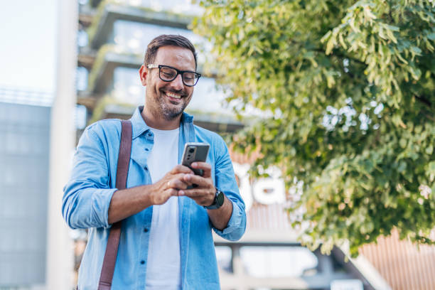 istock A handsome, cheerful, smiling man walking by a building, using smartphone. 2170786805