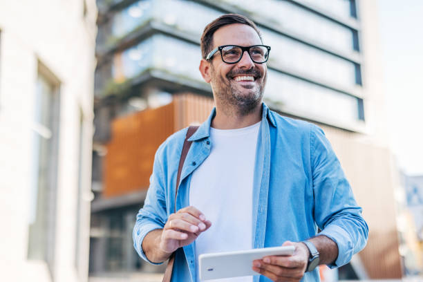 istock A handsome, cheerful, smiling man walking by a building, using tablet. 2170786895