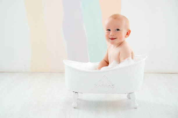 A baby boy is bathing in a bubble bath, a small child is playing with foam and splashes having fun and laughing.