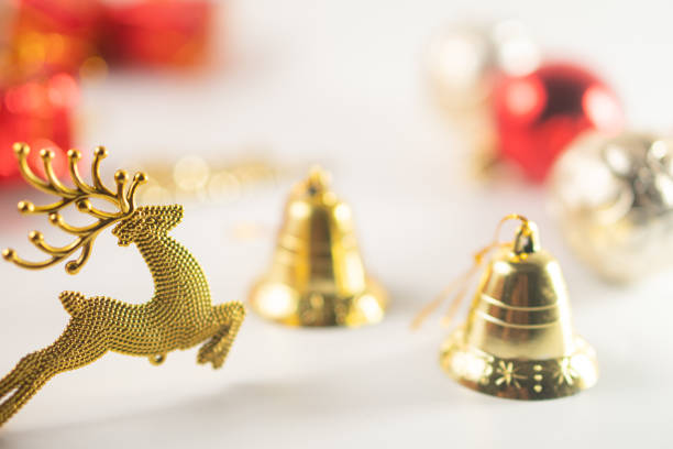 A festive arrangement featuring a golden reindeer figurine, two golden bells, and colorful Christmas ornaments in red and silver. The background is softly blurred, enhancing the holiday theme.