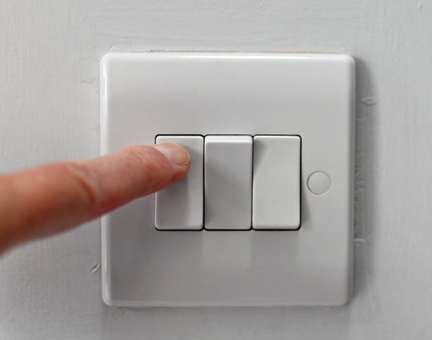 Electric wall mounted electric triple light switch being pushed by a finger