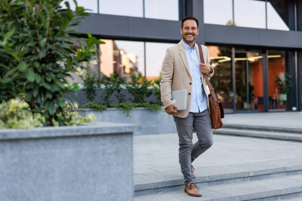istock Smiling man holding laptop near office building steps 2170817887