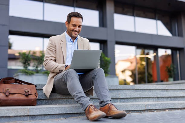 Smiling man sitting outside working on laptop stairs