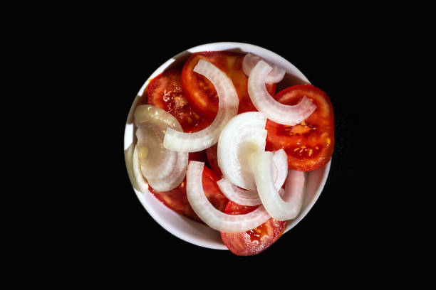 Tomato and onion salad in a bowl on a black background. Top view. Ideal for cooking and healthy eating content.