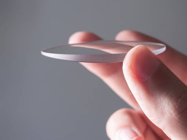hand holds a circular glass lens for eyeglasses