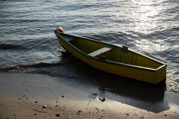 A yellow wooden boat resting on the shore with gentle waves and sunlight reflecting on the water.