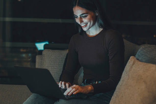 istock Young woman sitting on a hotel room sofa in the evening, using a laptop for remote work or chatting with friends and family. Embracing the modern digital nomad lifestyle and nighttime productivity 2170826731