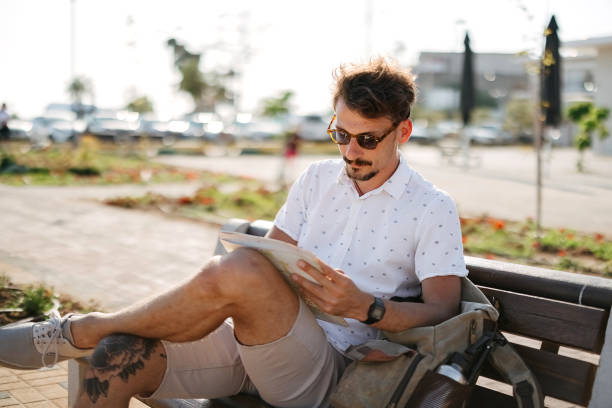 Happy male traveler making plan of journey while sitting on bench