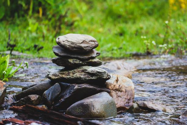 A peaceful stack of smooth stones balanced beside a flowing stream, nestled in nature's greenery
