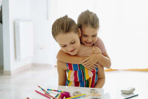 istock Two young sisters are sitting at a table doing arts and crafts, painting rocks and using colorful markers in a bright room. 2170833688