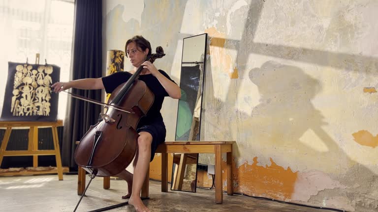 A middle-aged, white female musician wearing a black dress is playing the cello in an old building