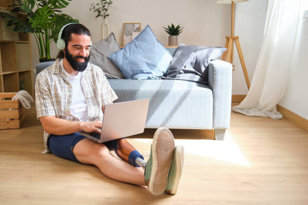 istock Smiling young man with prosthetic leg working on laptop at home 2170845441