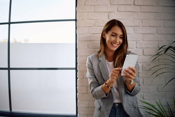 istock Happy female entrepreneur using smart phone while standing by the window in the office. 2170849425