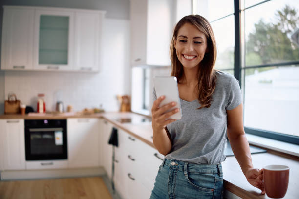 istock Happy woman using cell phone while drinking coffee in the kitchen. 2170849511