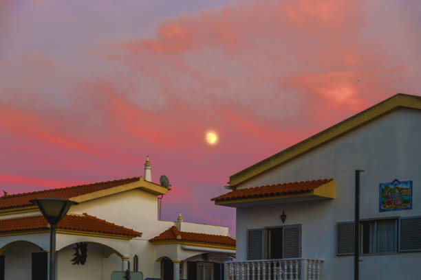 Moonlight shining through colorful evening clouds above suburban homes.