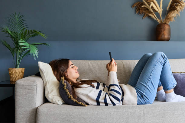 istock Beautiful woman is lying on a comfortable sofa, enjoying a relaxing moment at home while browsing on her smartphone 2170863344