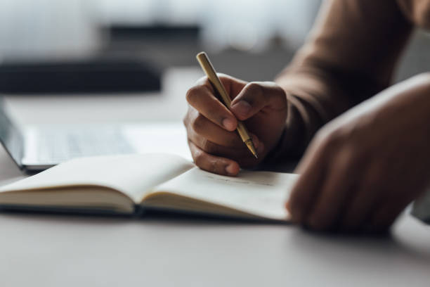 Close-Up of Hand Writing with Pen on Notebook