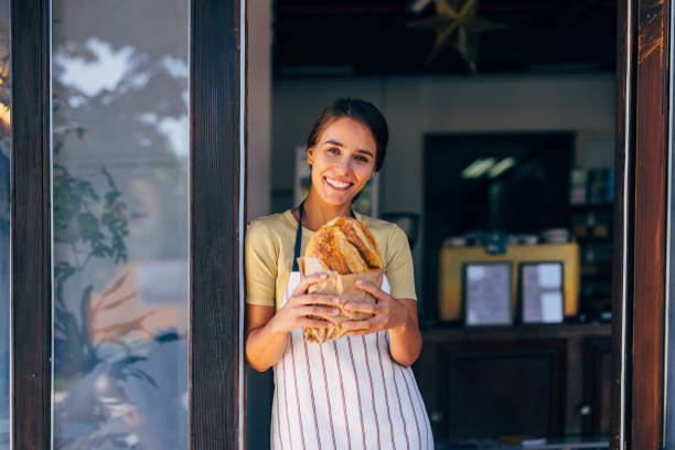 istock Smiling Female Baker Holding Fresh Bread at Bakery Entrance 2170880556