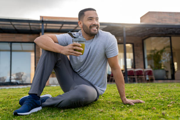 Healthy young man drinking a green smoothie and smiling while sitting outdoors - healthy lifestyle concepts