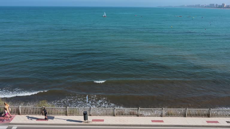 Strollers along Campello Beach, Costa Blanca, Alicante, with expansive water extending to the distant horizon.